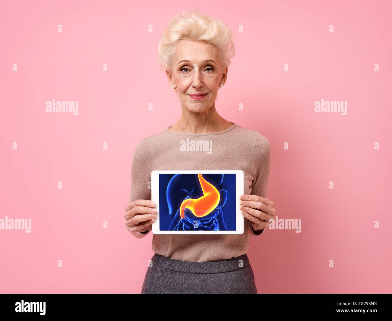 Femme attrayante montre l'image de la radiographie de l'estomac. Photo d'une femme âgée souriante avec une tablette dans les mains sur fond rose. Conc. Médicale Banque D'Images