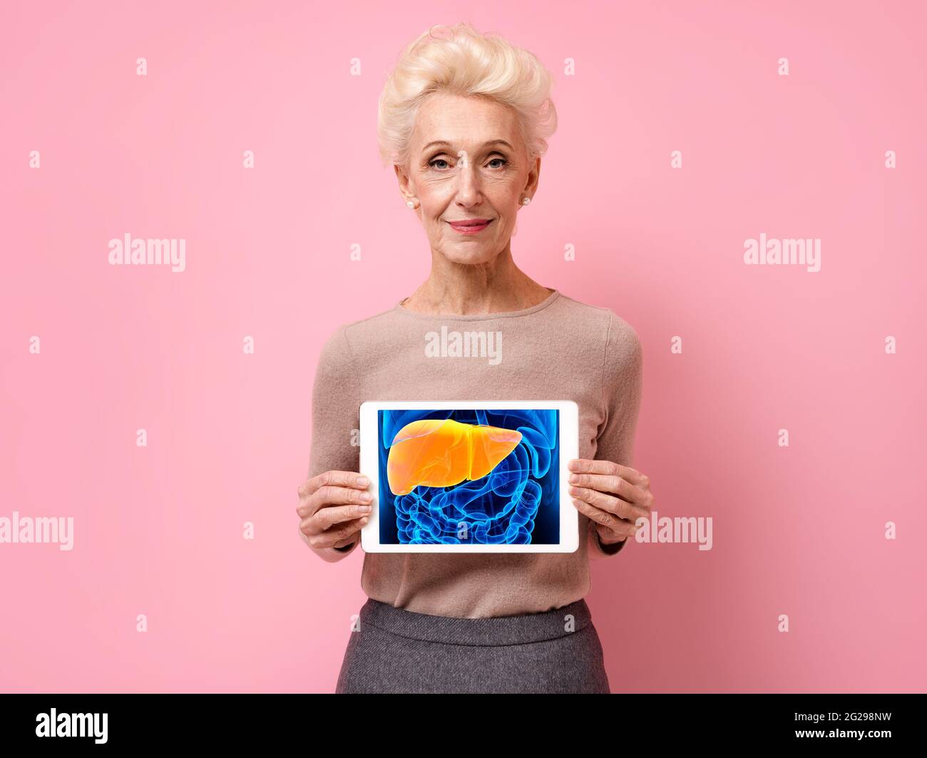 Une femme attirante montre l'image radiologique du foie. Photo d'une femme âgée souriante avec une tablette dans les mains sur fond rose. Concept médical Banque D'Images