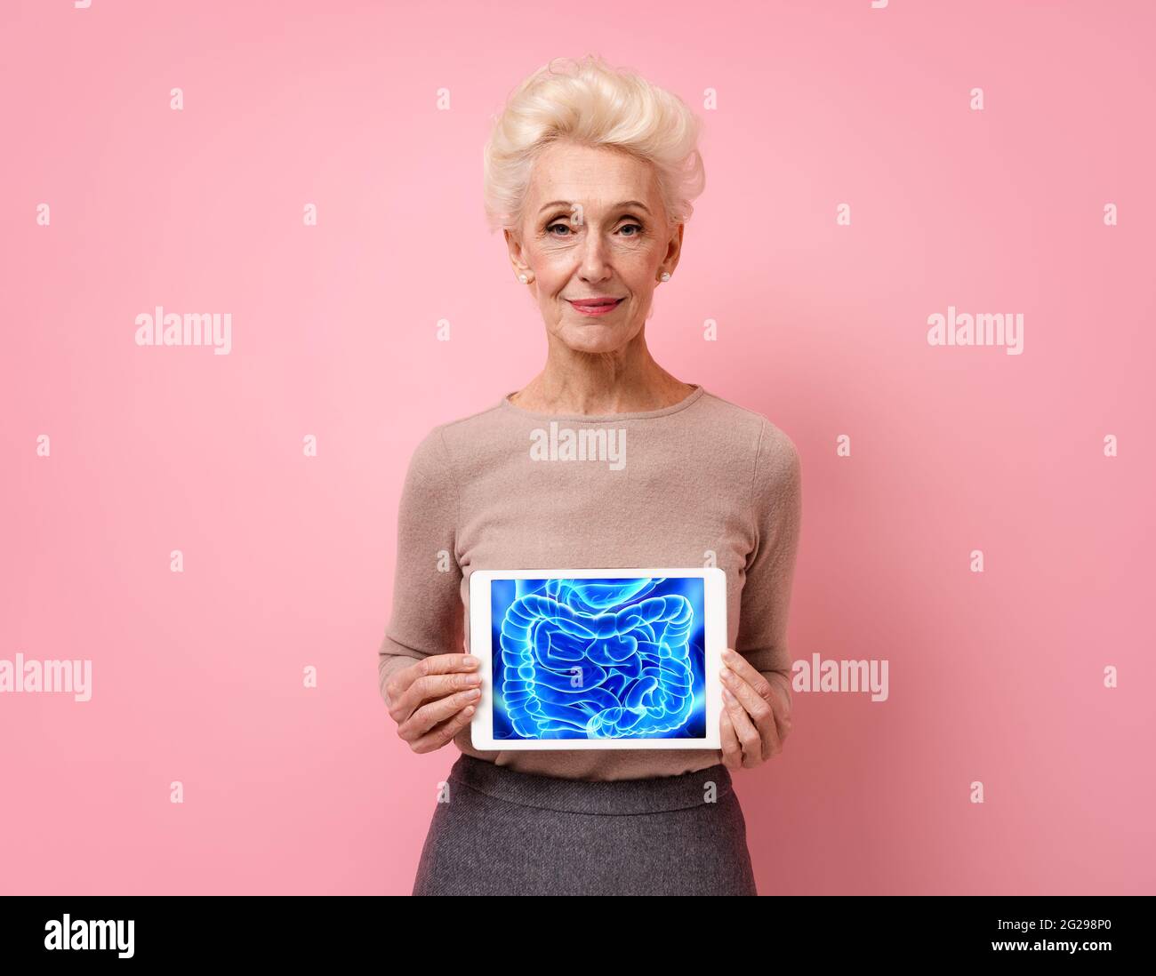 Femme attrayante montre l'image de la radiographie des intestins. Photo d'une femme âgée souriante avec une tablette dans les mains sur fond rose. Médical c Banque D'Images