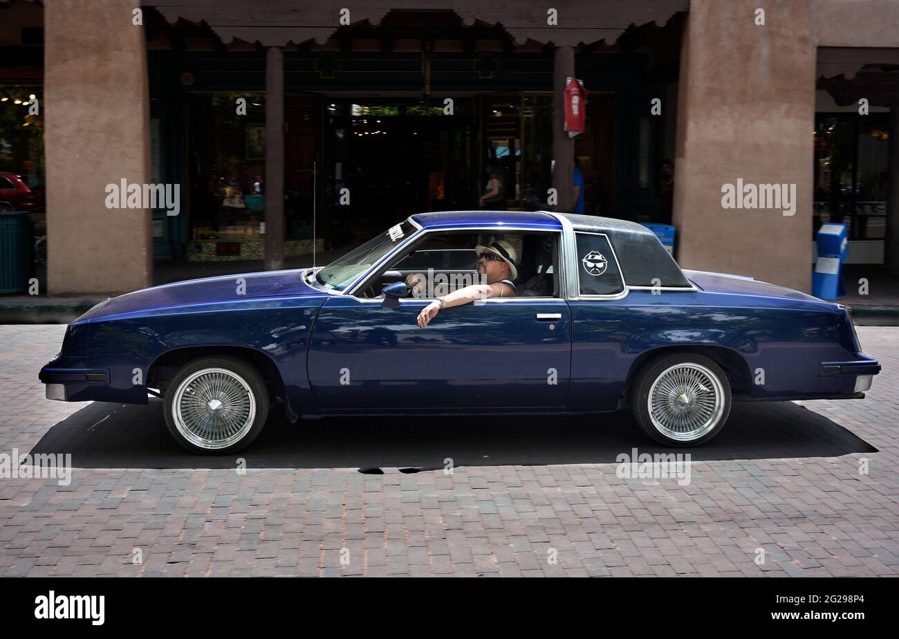 Un hispanique avec une voiture basse personnalisée navigue à travers la place historique de Santa Fe, Nouveau-Mexique. Banque D'Images