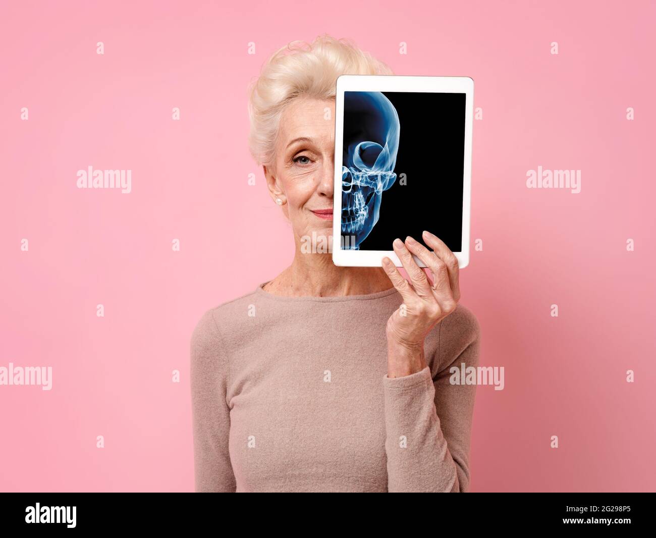 Une femme attirante présente des rayons X du crâne. Photo d'une femme âgée souriante avec une tablette dans les mains sur fond rose. Concept médical Banque D'Images