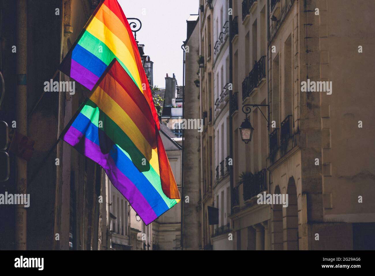 Deux drapeaux LGBTQ accrochés au coin du bâtiment ancien pendant la fierté de Paris. Symbole de culture LGBTQIA. Drapeaux gais lumineux agitant dans le vent à la journée ensoleillée à Paris, Banque D'Images