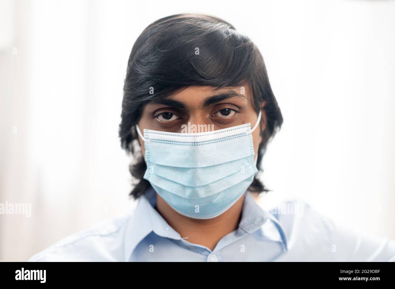 Portrait en gros plan d'un jeune indien sérieux portant un masque médical chirurgical et une chemise bleue élégante et décontractée, l'homme de l'est se protège contre les maladies virales, empêchant la propagation du virus corona Banque D'Images