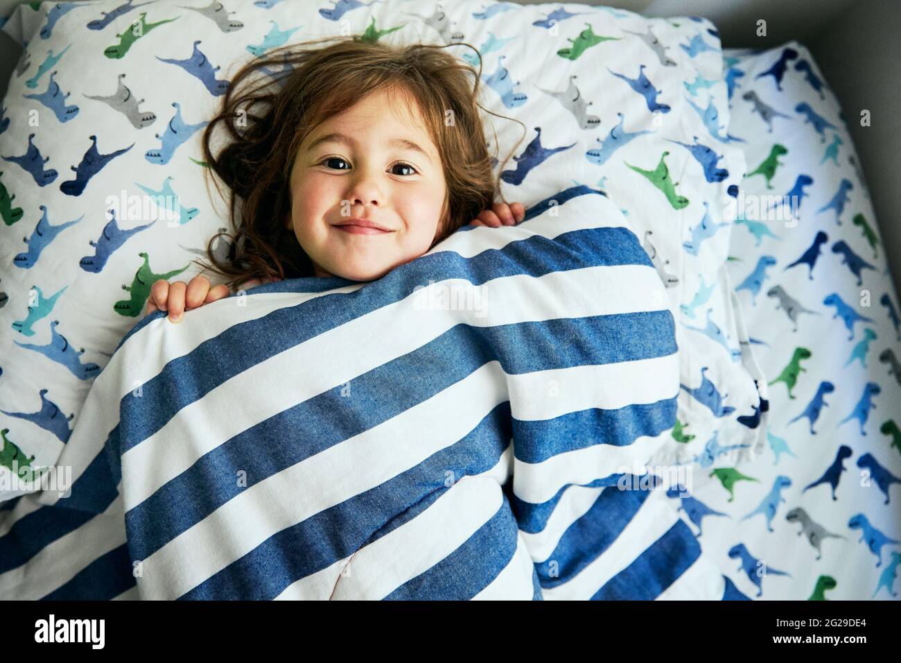 Portrait d'une jolie fille recouverte d'une couverture couchée sur le lit à la maison Banque D'Images