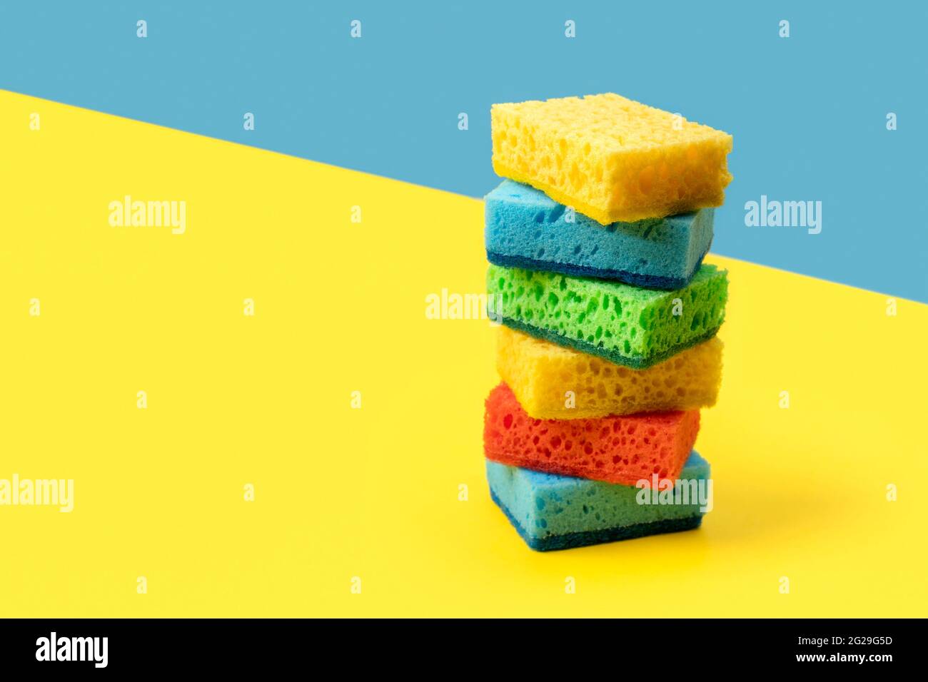 Disposition créative avec éponges pour le lavage de la vaisselle sur fond jaune et bleu Banque D'Images