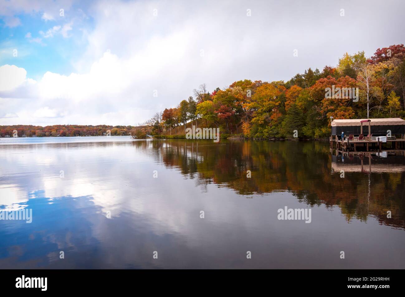 Le vent est calme sur un lac du Wisconsin en automne. Les couleurs des arbres et du ciel partiellement nuageux se reflètent à la surface du lac. Banque D'Images