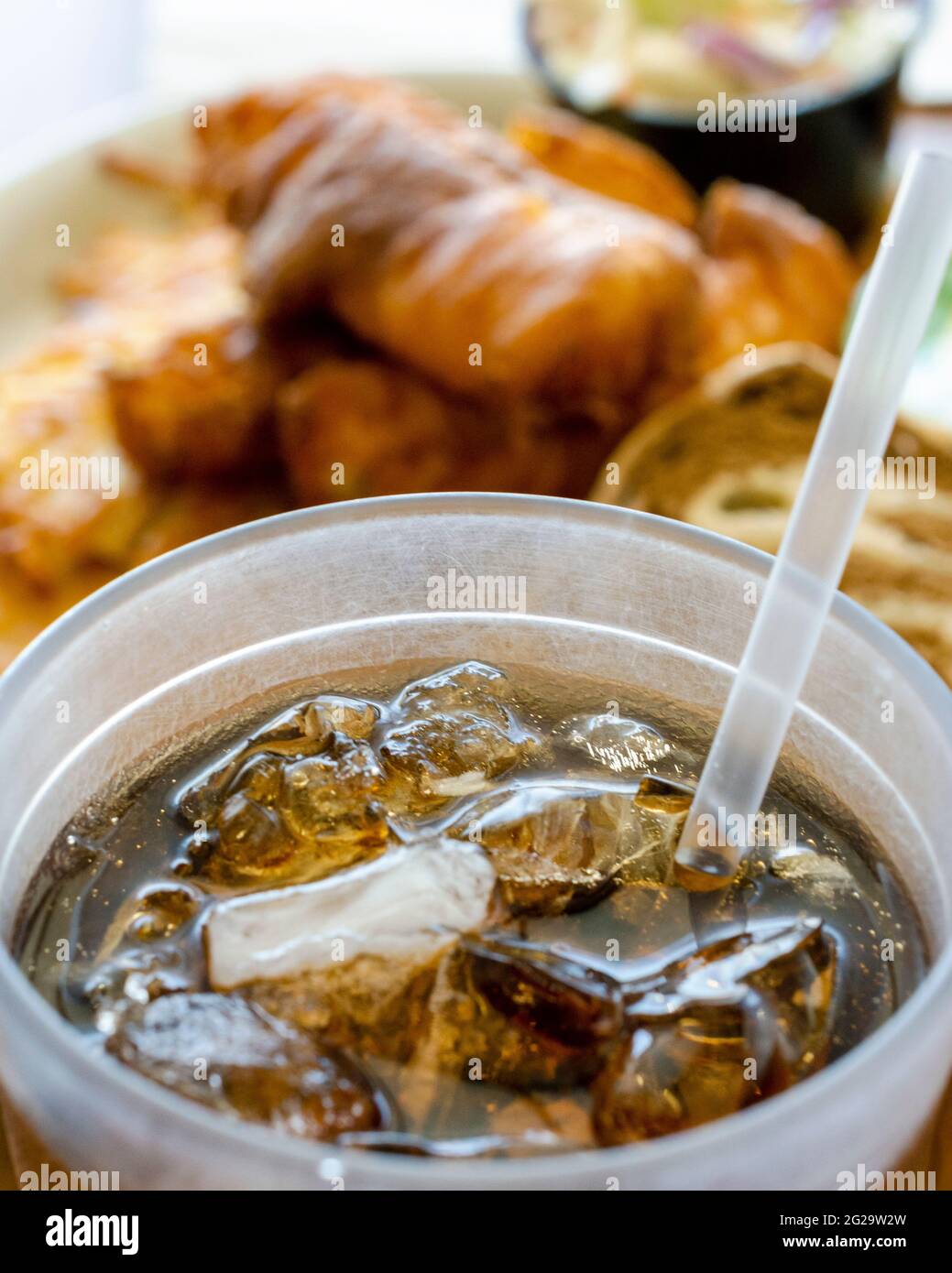 Mise au point sélective sur un grand verre en plastique de soda avec de la glace et une paille. Repas flou en arrière-plan. Paramètre Diner. Banque D'Images