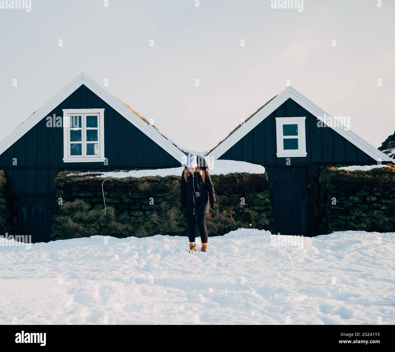Femme pleine longueur en vêtements de dessus debout sur la neige près de belles cottages contre le ciel gris le jour d'hiver en Islande Banque D'Images