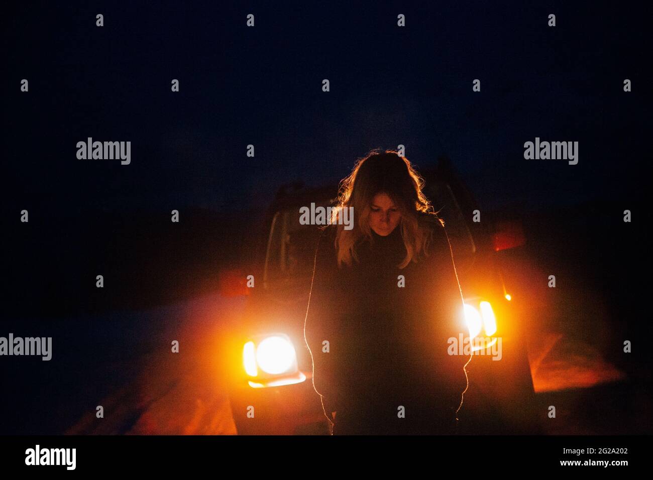 Femme voyageur debout devant la voiture avec des phares lumineux pendant le voyage dans la campagne enneigée la nuit en Islande Banque D'Images