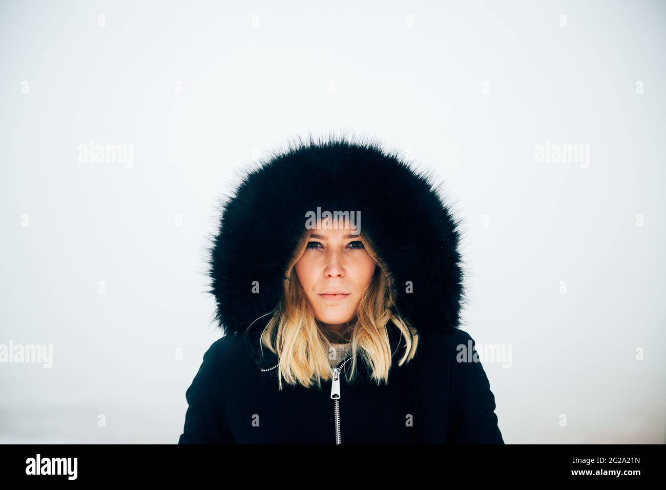 Blonde mignonne en vêtement chaud à capuche regardant l'appareil photo contre le ciel gris dans la campagne le jour d'hiver en Islande Banque D'Images