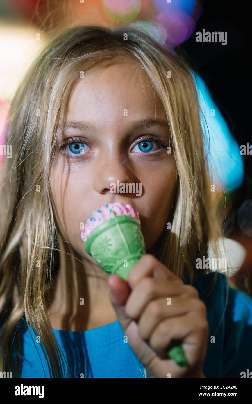 Petite fille blonde mangeant une délicieuse crème glacée dans le parc d'attractions la nuit Banque D'Images