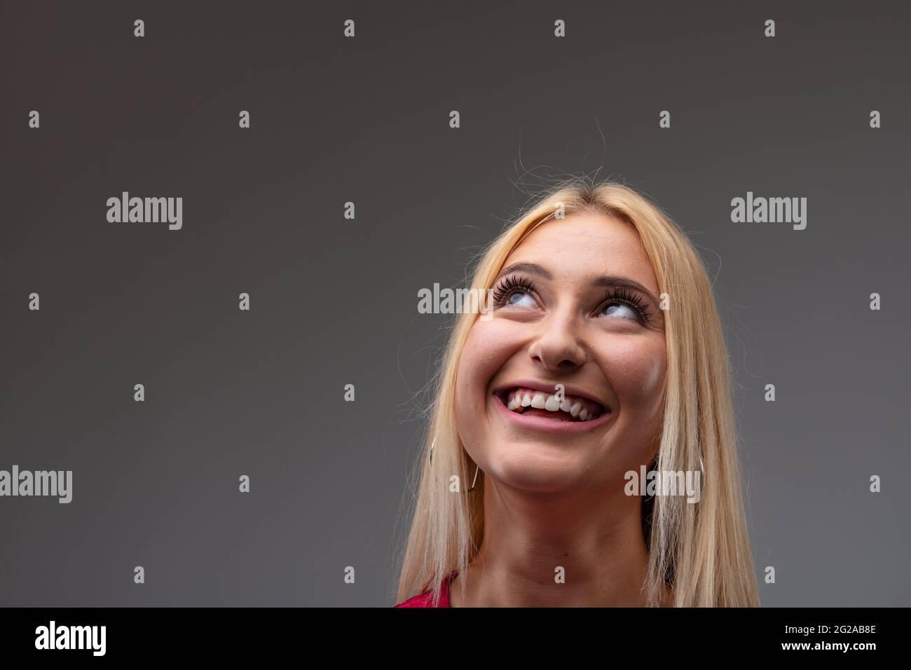 Jolie jeune femme blonde debout rêve avec un sourire heureux et les yeux élevés à l'espace d'imitation dans un portrait de tête tourné sur un fond gris studio Banque D'Images