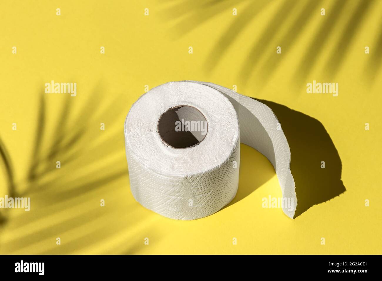 rouleau de papier toilette blanc isolé sur un fond jaune sous une ombre de palmier gros plan. ombres dures du soleil à midi Banque D'Images