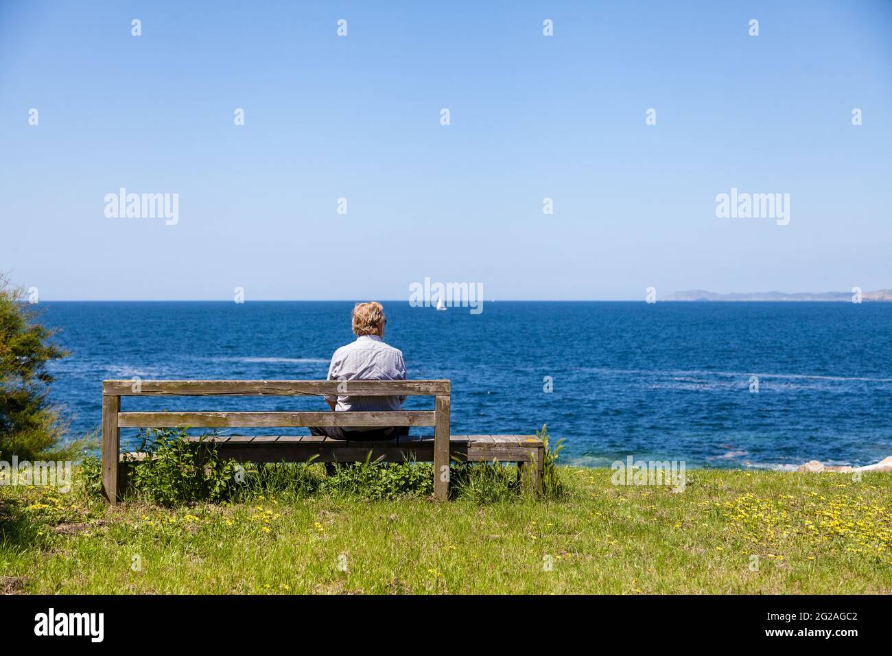 Un homme, assis au bord de l'océan, seul, face à l'extérieur de la caméra, appréciant, contemplant la vue Banque D'Images