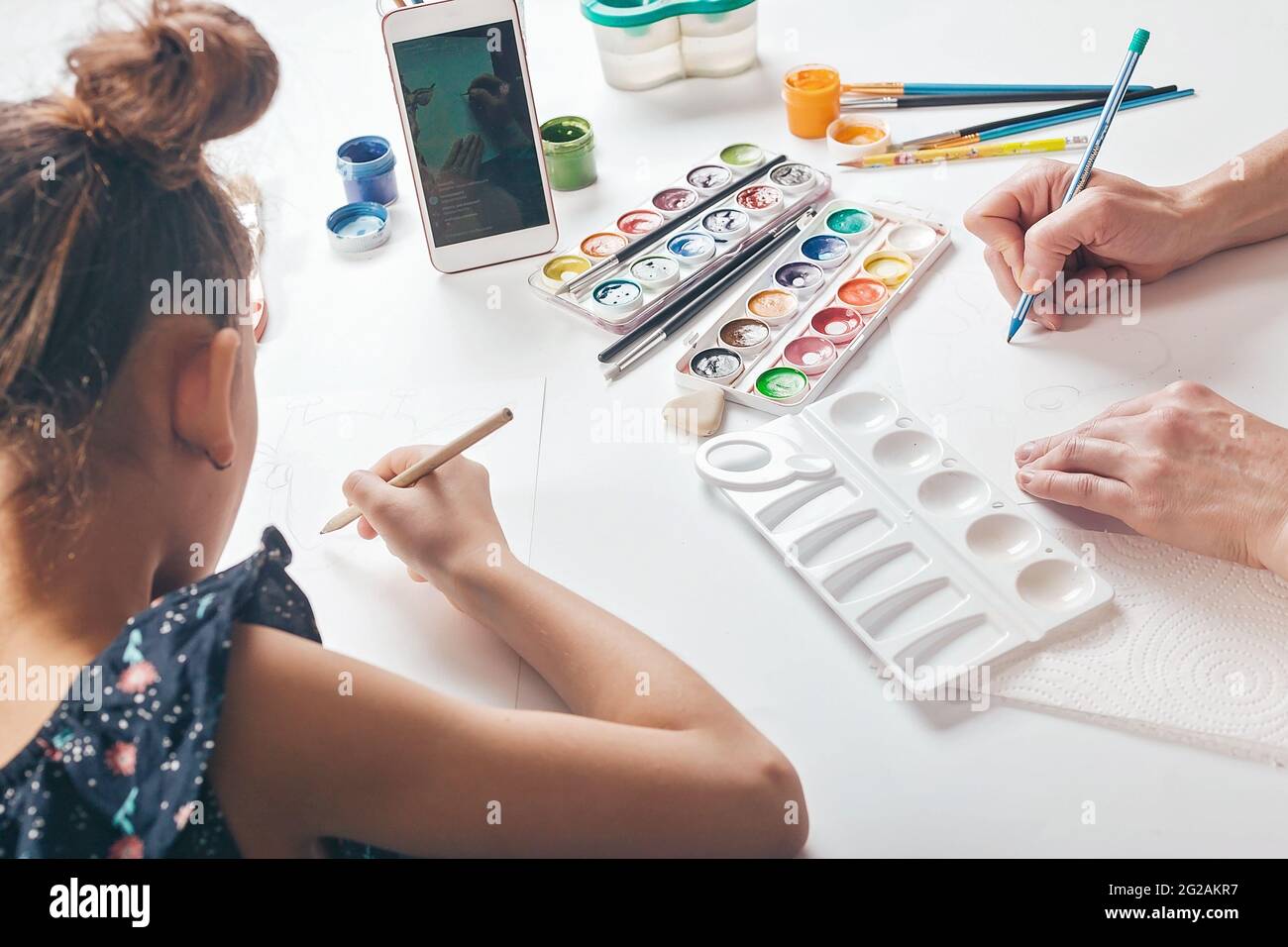 Une mignonne écolière s'assoit à une table avec sa mère et regarde une leçon de dessin en ligne. L'utilisation de la technologie Internet et en ligne dans la vie quotidienne. Li Banque D'Images