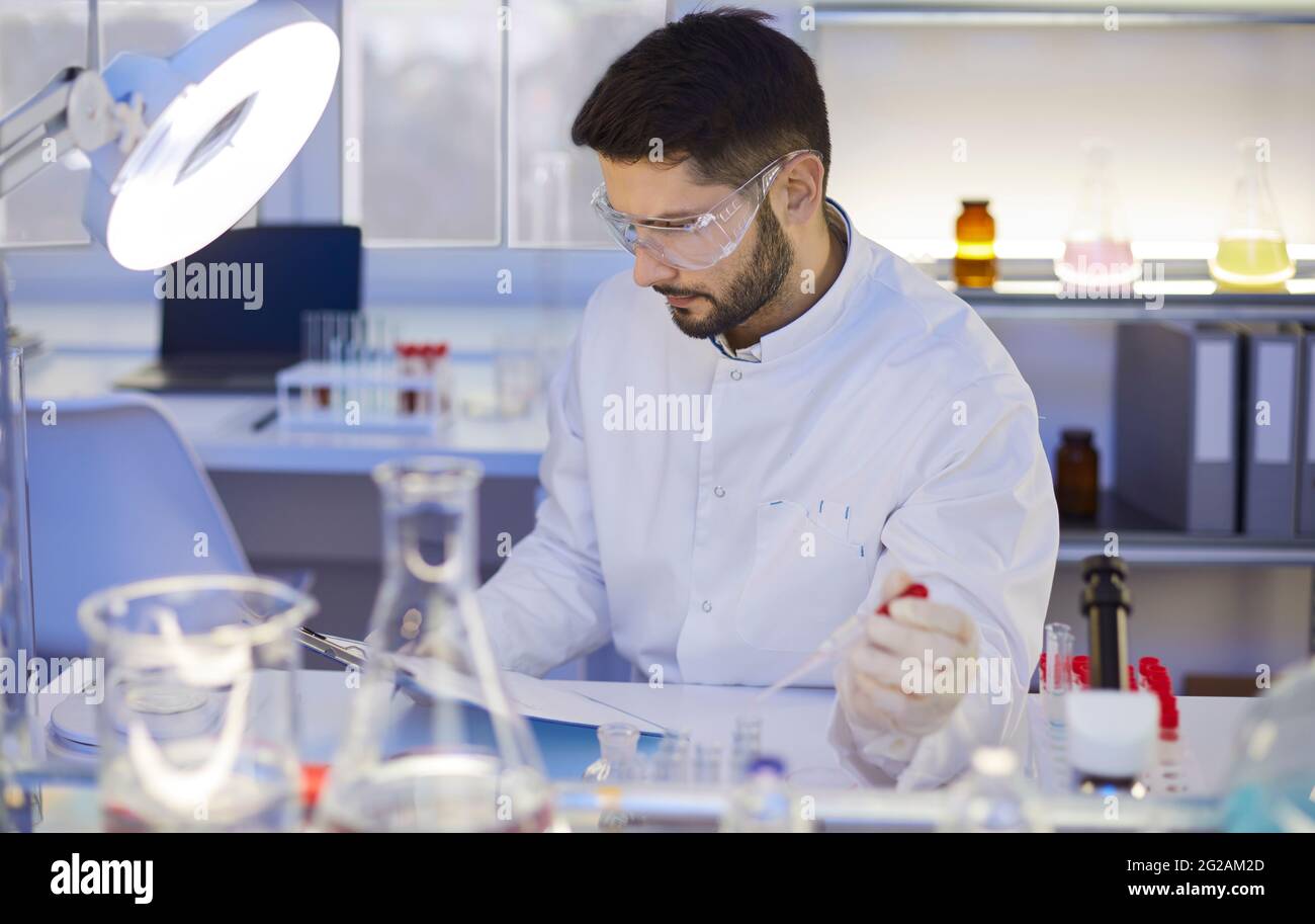 Scientifique en blouse de laboratoire et lunettes de protection lisant le papier de recherche scientifique en laboratoire Banque D'Images