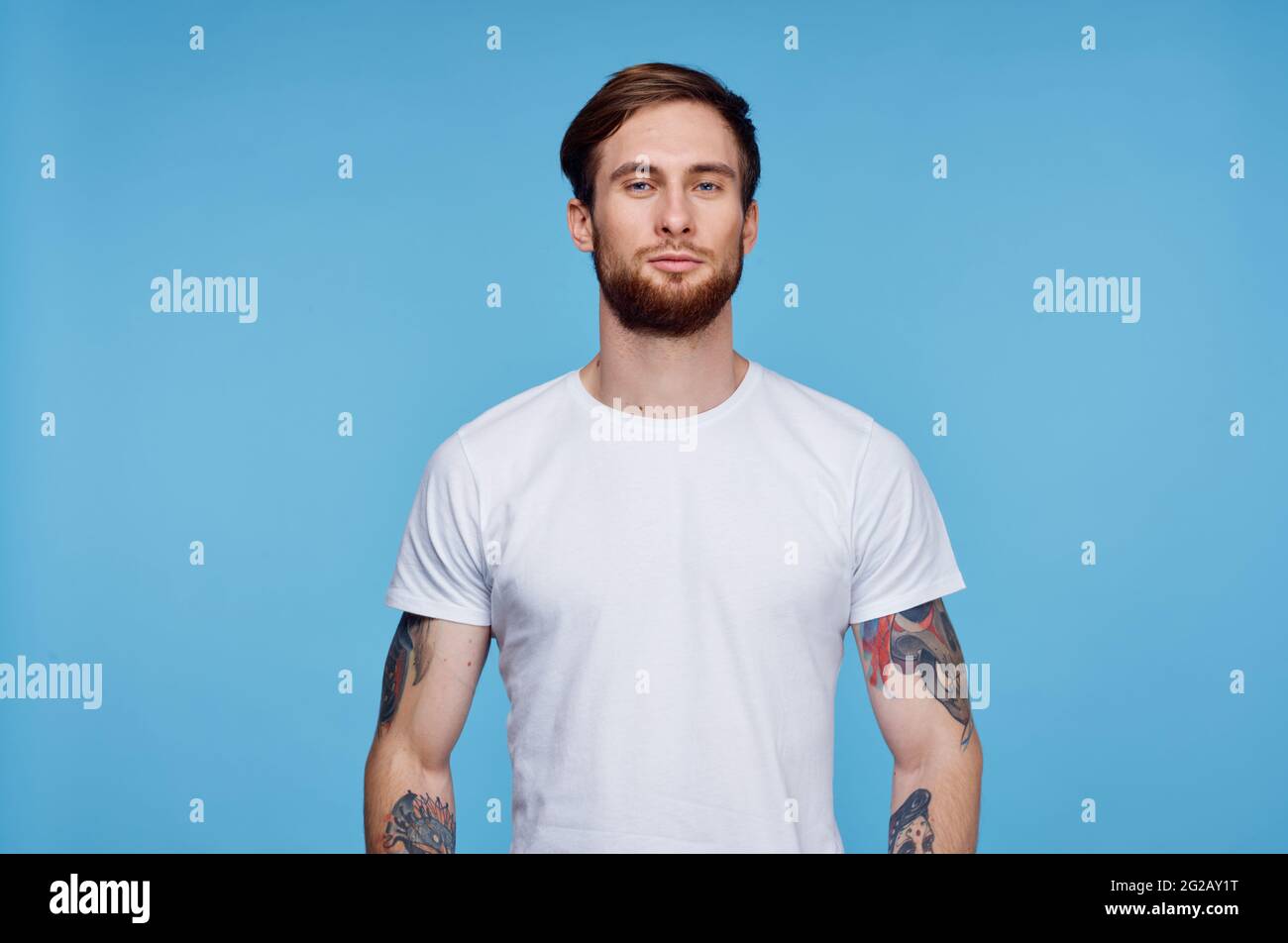 beau homme en t-shirt blanc tatouages sur ses bras court afficher l'arrière-plan bleu Banque D'Images