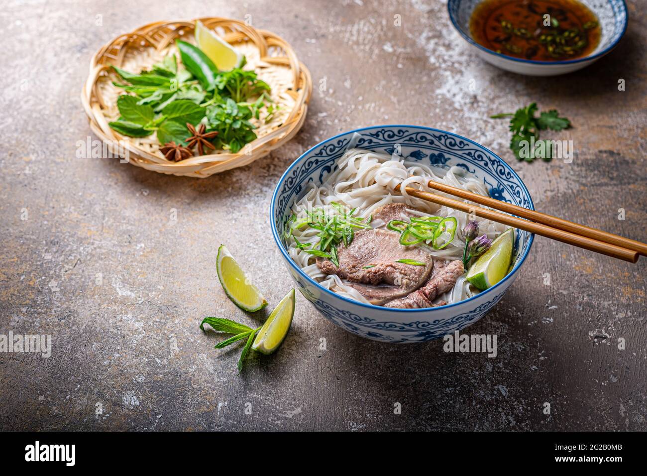 Soupe vietnamienne traditionnelle de nouilles pho dans un bol, garni de basilic, menthe, citron vert, sur fond de béton. Banque D'Images