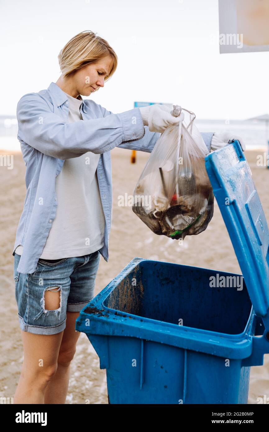 Une jeune femme bénévole jette un sac à ordures dans une poubelle sur la  plage Photo Stock - Alamy