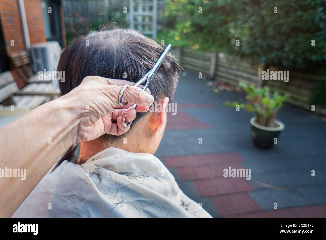 Un homme obtient une coupe de cheveux à la maison dans l'arrière-cour - soins de cheveux, coupe de cheveux, concept d'auto-isolation. Banque D'Images