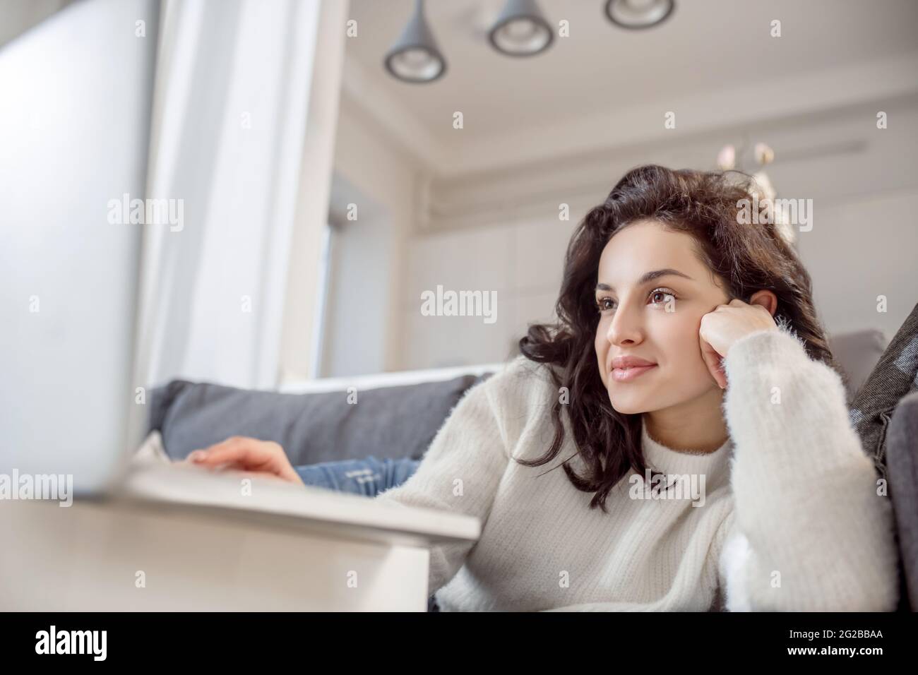 Une femme décontractée en chandail blanc allongé sur le canapé et regardant quelque chose en ligne Banque D'Images