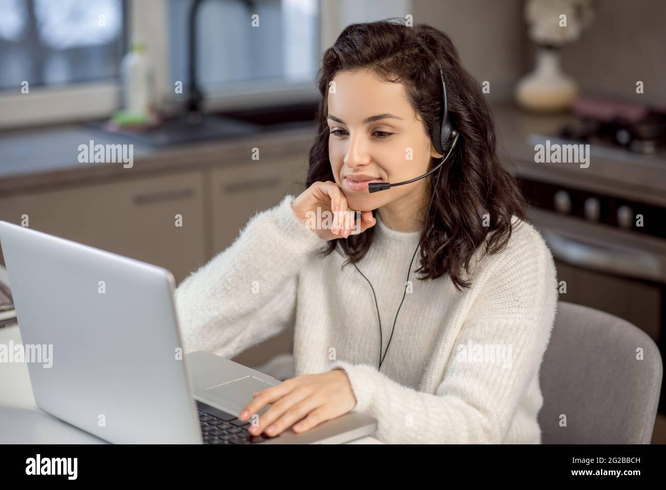 Une femme dans des écouteurs assis à l'ordinateur portable tout en travaillant de la maison Banque D'Images