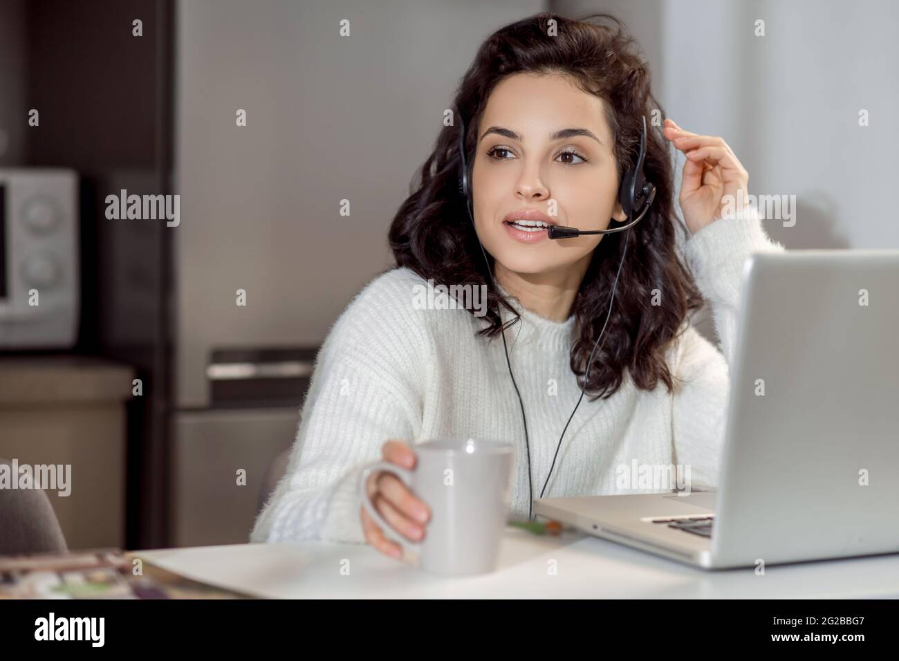 Une femme dans des écouteurs assis à l'ordinateur portable tout en travaillant de la maison Banque D'Images