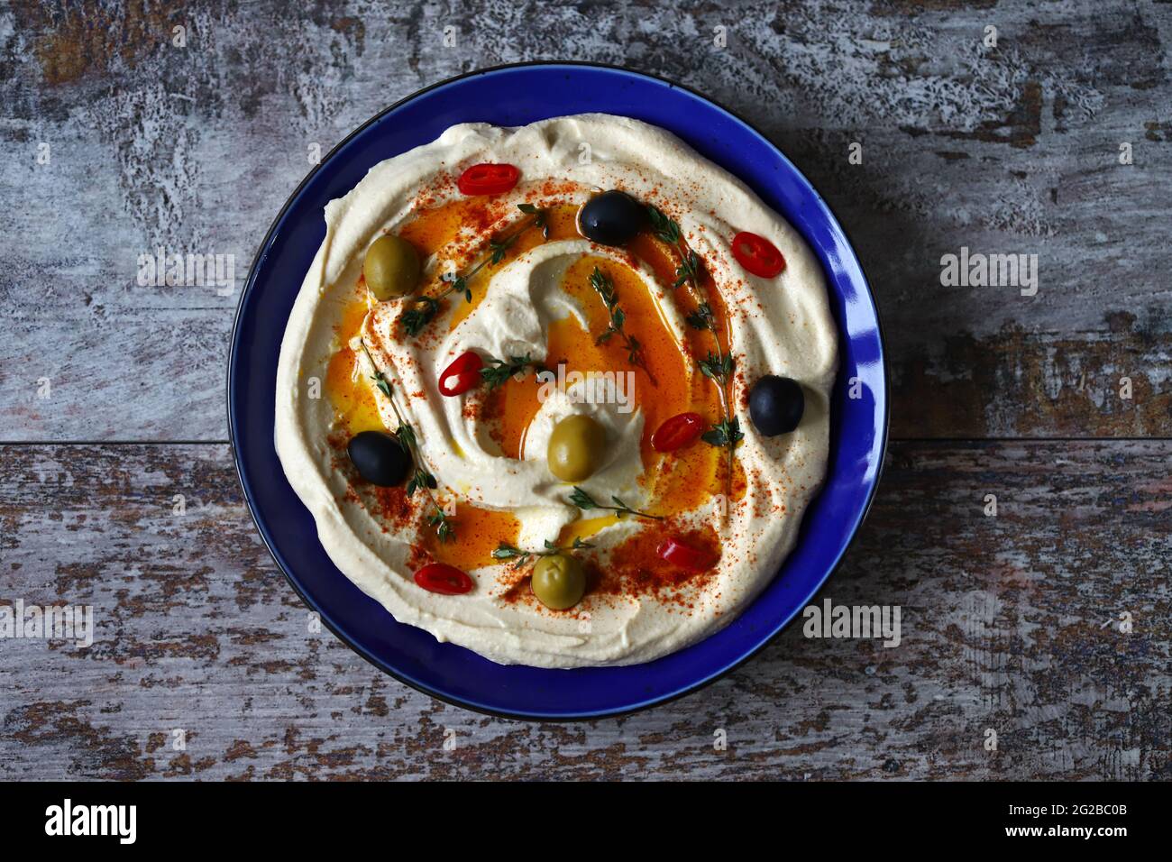 Houmous aux olives, paprika et huile d'olive dans une assiette bleue. Une collation traditionnelle du Moyen-Orient. Banque D'Images