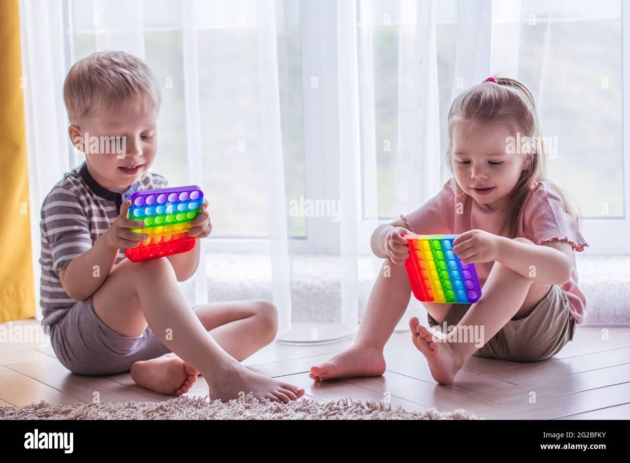 Blonde garçon et fille les enfants jouent avec le jouet sensoriel pop IT. Jeu de fidgeting de silicium tendance pour les enfants et les adultes stressés. Jouets à bulles souples et accroupés. Enfant p Banque D'Images