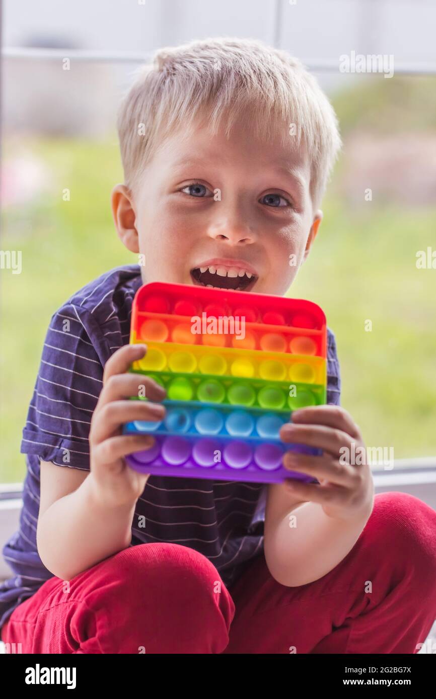 Un petit garçon blond est assis et regarde la caméra avec un jouet popit  moderne coloré et lumineux simple bosselure. L'enfant avec des antistress s  tendance colorés Photo Stock - Alamy