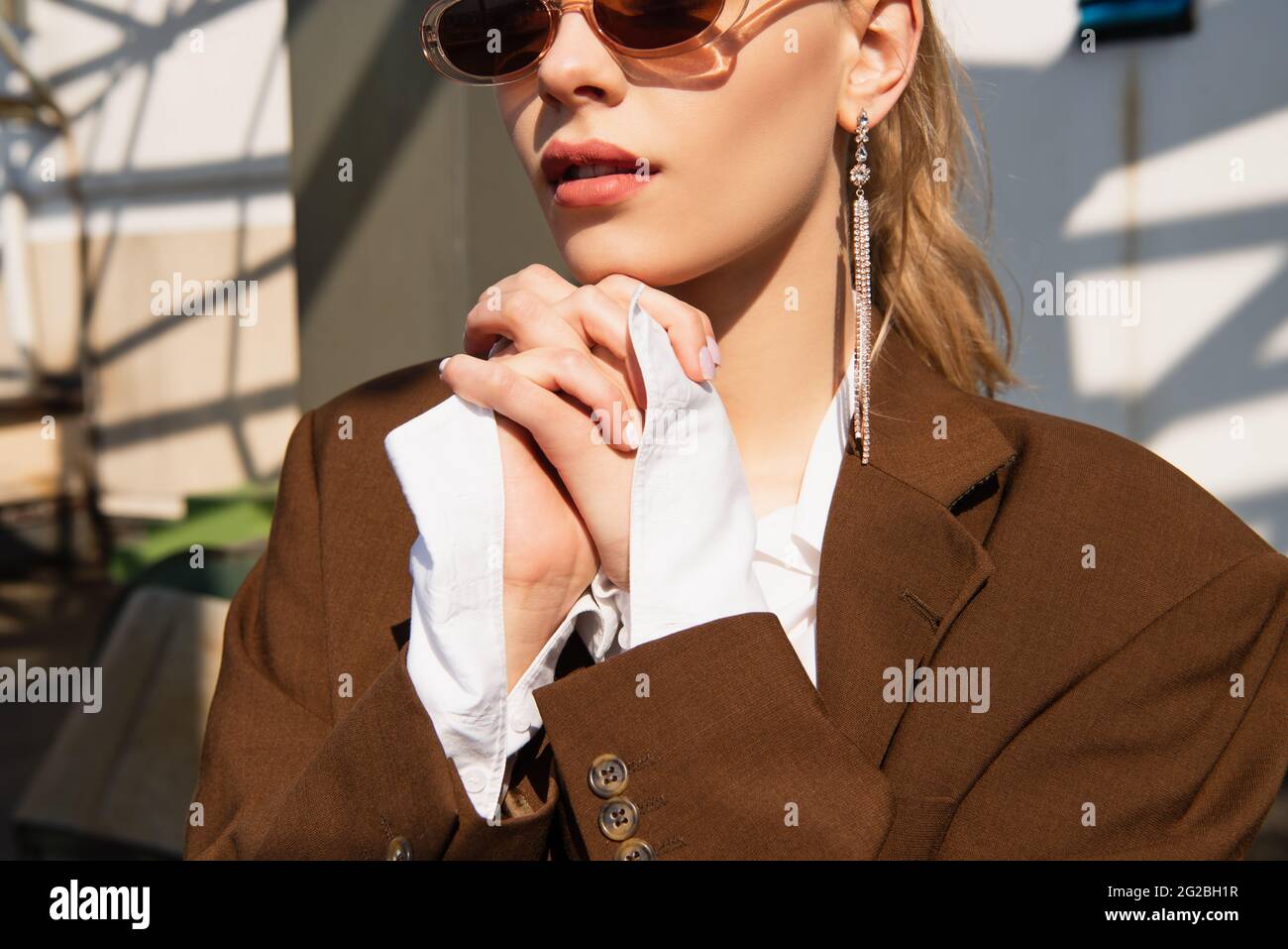 jeune modèle avec boucles d'oreilles et lunettes de soleil posant avec les  mains serrées Photo Stock - Alamy