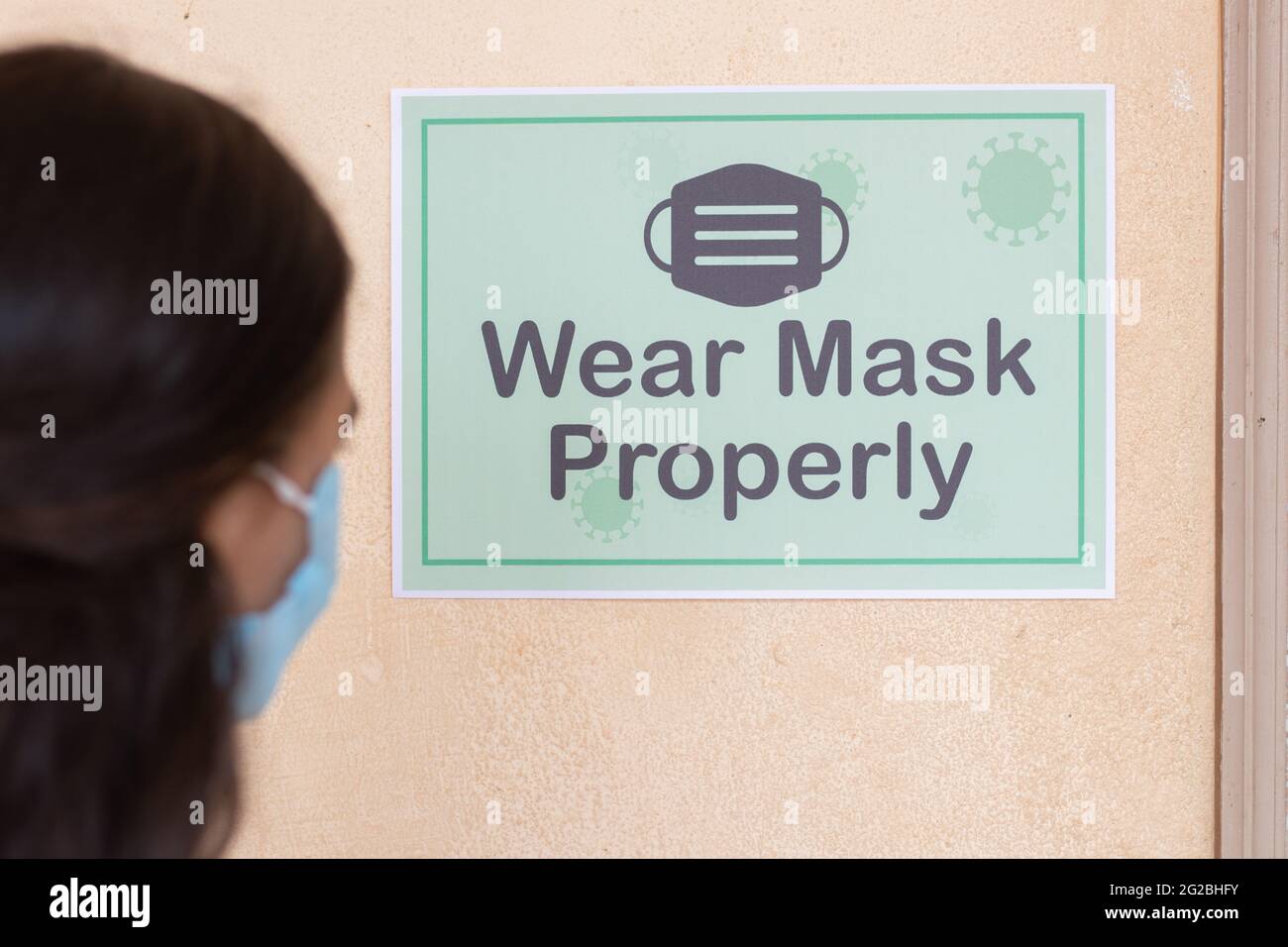 Prise de vue en bandoulière de la jeune fille élève ajustement du masque en voyant le masque de port correctement avis sur le mur de la salle de classe avant d'entrer en classe pour protéger Banque D'Images