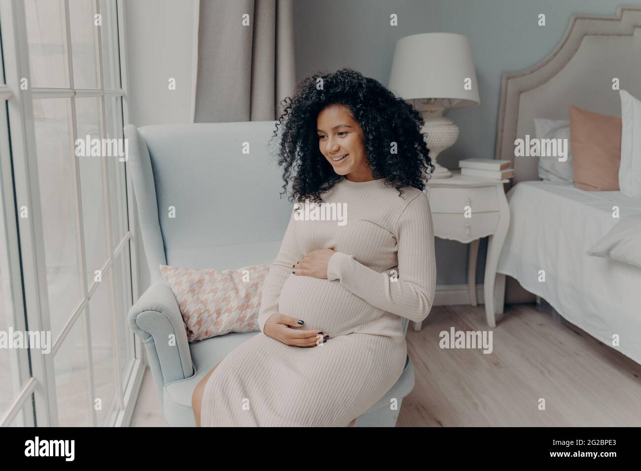 Charmante femme enceinte afro-américaine regardant dans la fenêtre et pensant au futur bébé Banque D'Images