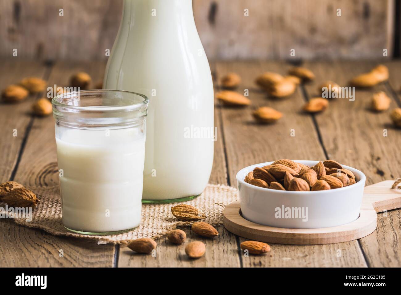 Verre et pichet au lait d'amande vegan, amandes entières et amandes entières sur une ancienne table rustique en bois Banque D'Images