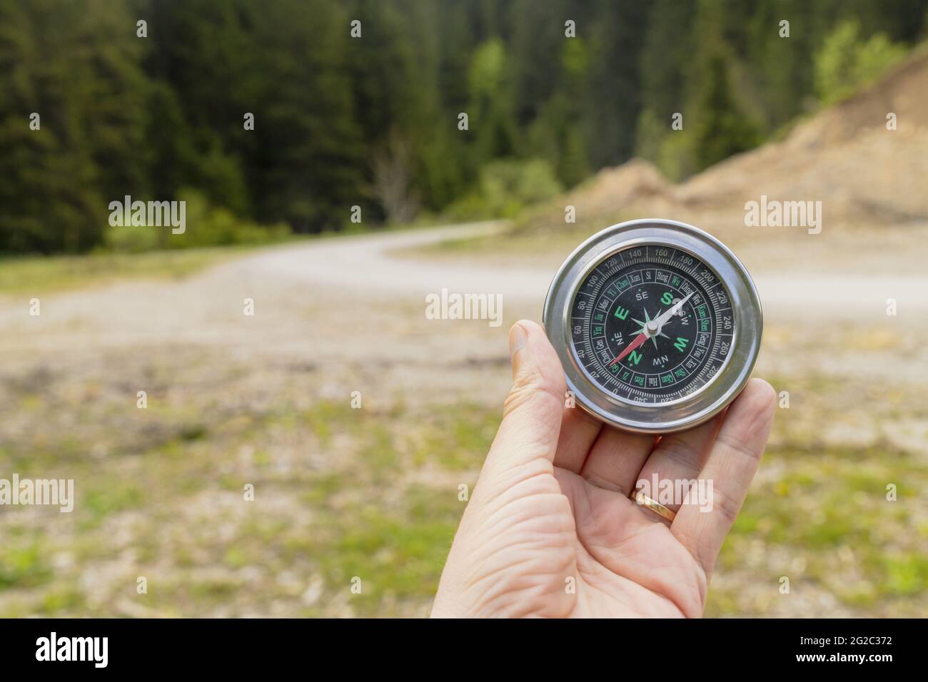 Main d'un alpiniste tenant une boussole avec un champ vert sur l'arrière-plan Banque D'Images