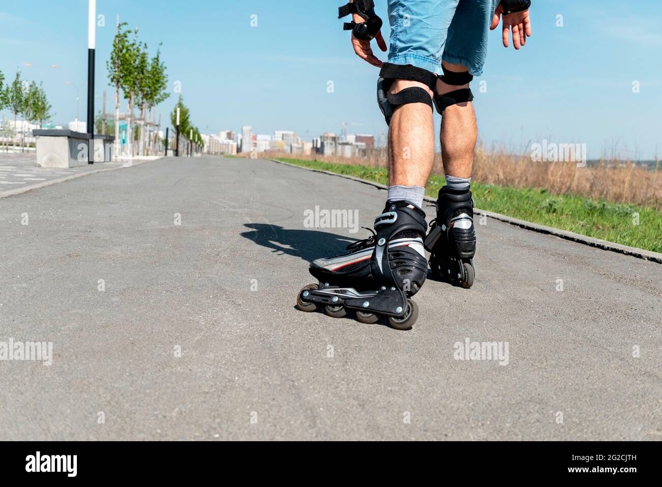 Jambes de sexe masculin dans des patins à roulettes et équipement de protection en gros plan sur la route asphaltée en été, roller, activité en plein air, sain Li actif Banque D'Images