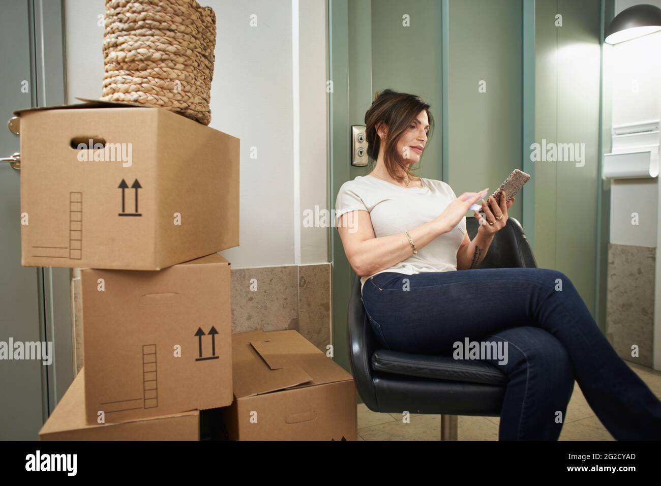 Femme mûre assise à côté de la pile de boîtes et en utilisant le téléphone Banque D'Images