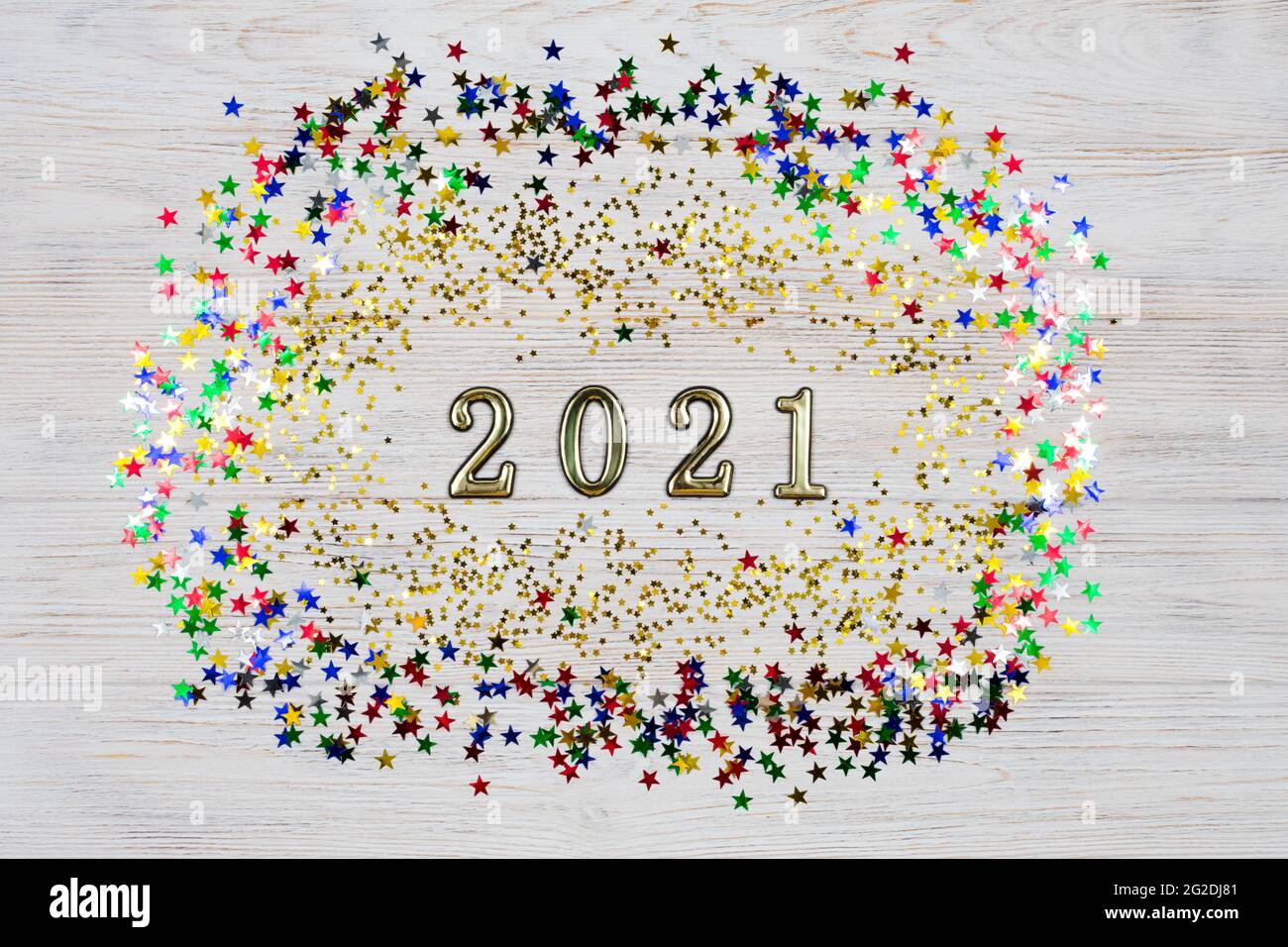 Golden Numbers 2021 entouré d'étoiles dorées et colorées sur fond de bois clair. Le symbole de la nouvelle année. Célébration du nouvel an 2021. Banque D'Images