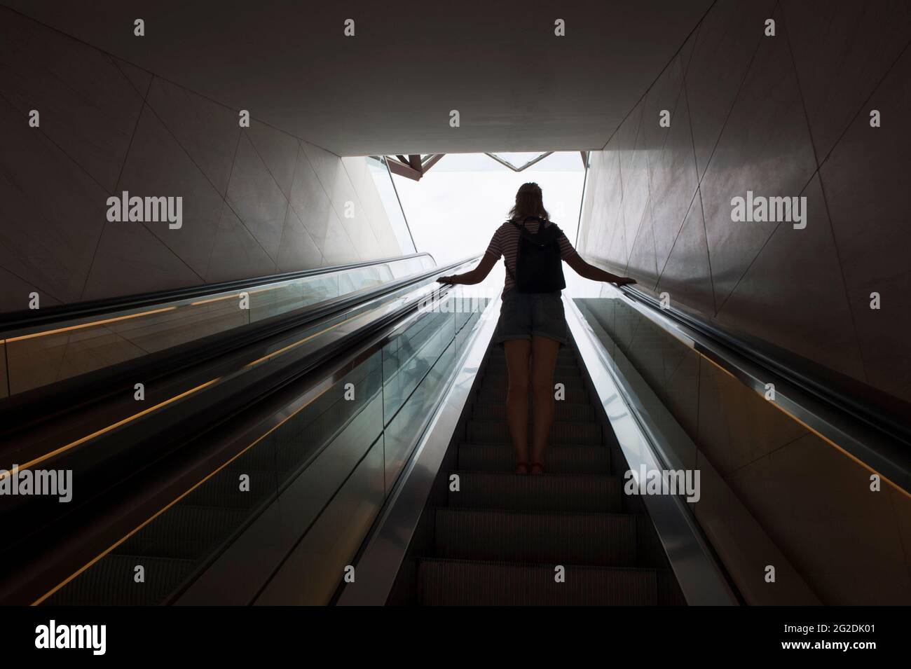 Une femme voyage sur un escalier mécanique dans un bâtiment moderne. Banque D'Images