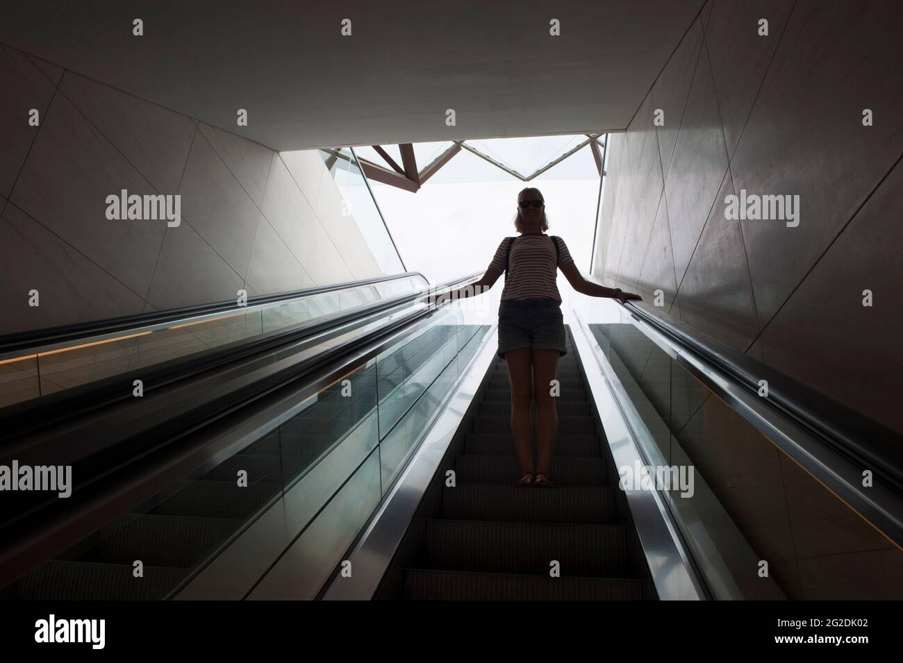 Une femme voyage sur un escalier mécanique dans un bâtiment moderne. Banque D'Images