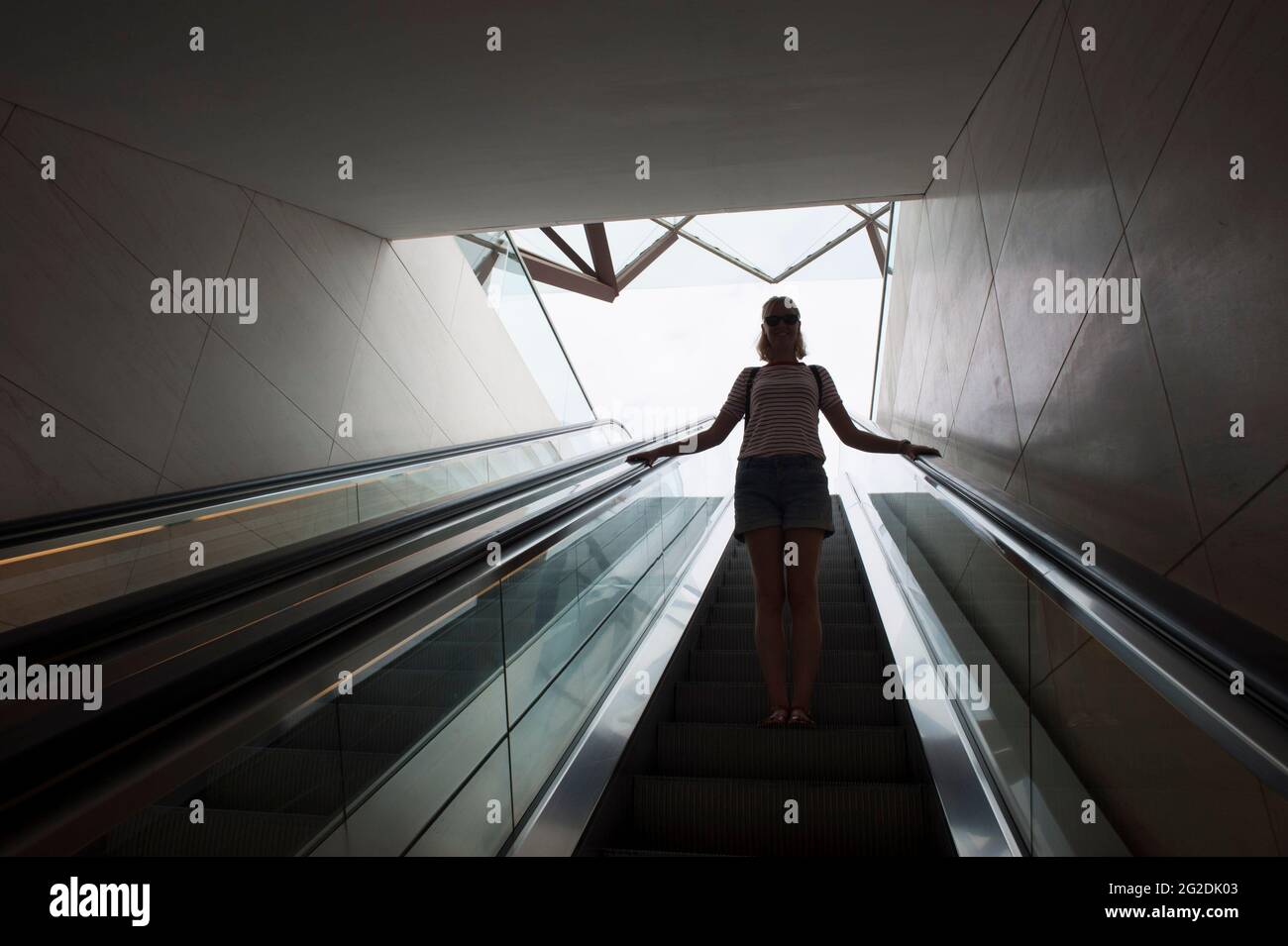 Une femme voyage sur un escalier mécanique dans un bâtiment moderne. Banque D'Images