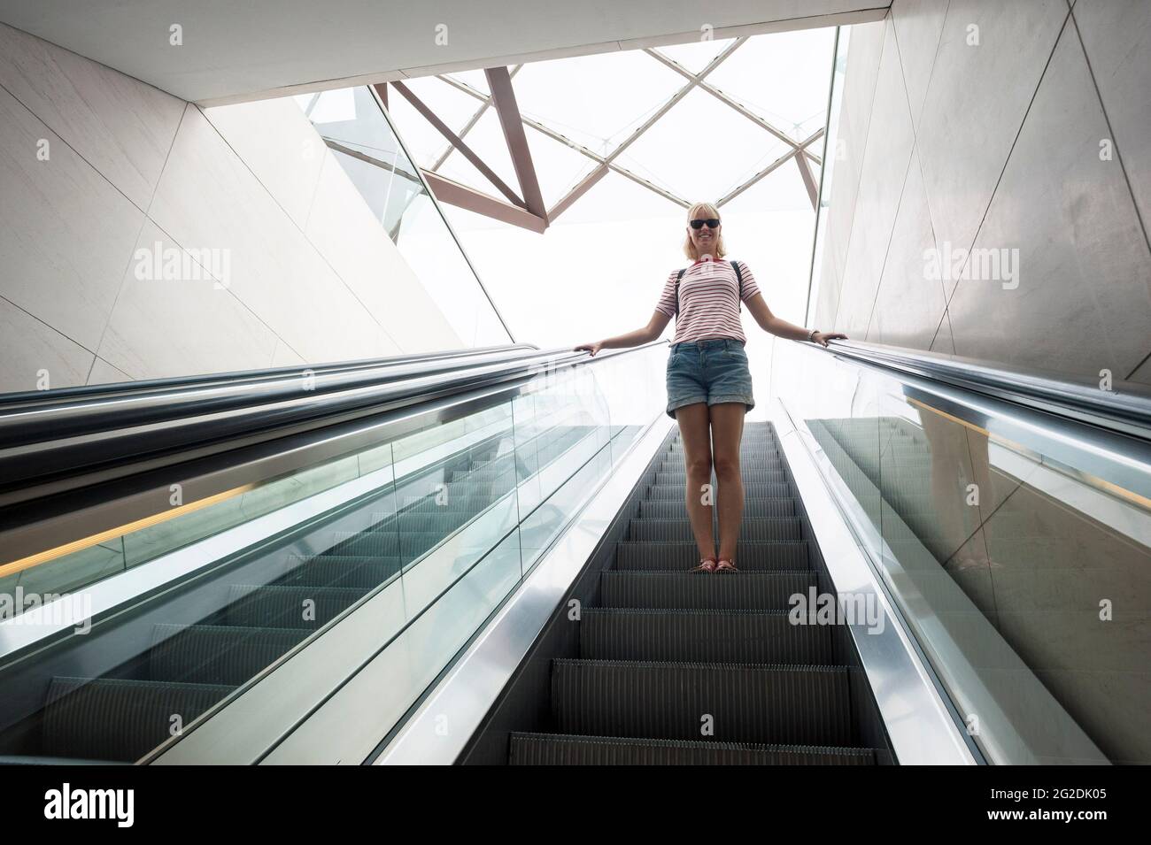 Une femme voyage sur un escalier mécanique dans un bâtiment moderne. Banque D'Images