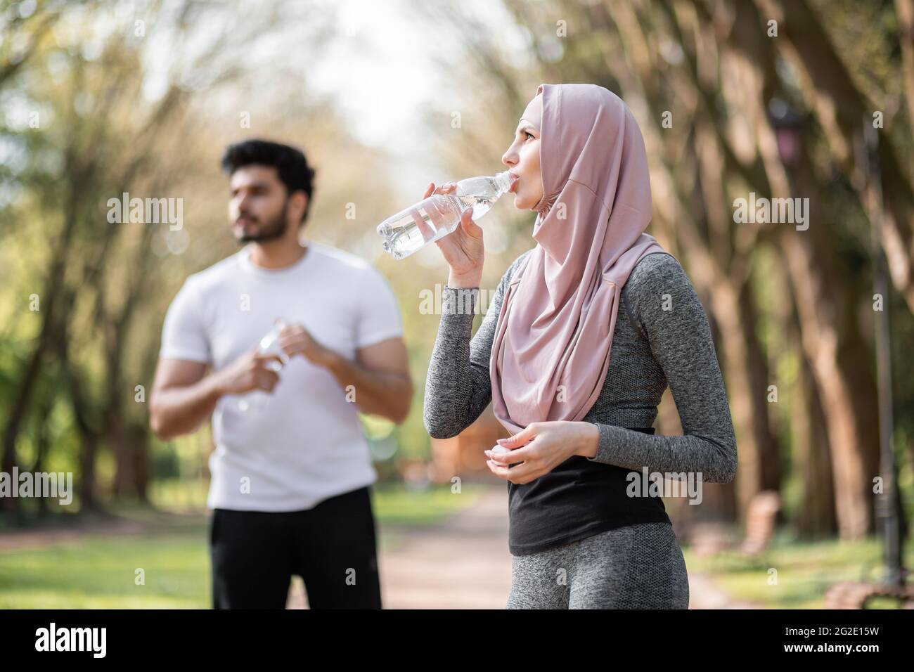 Vue latérale d'une femme attirante dans l'eau potable de hijab tout en un  bel homme arabe debout derrière. Jeune couple dans les vêtements de sport  se détendre après l'entraînement sur l'air frais