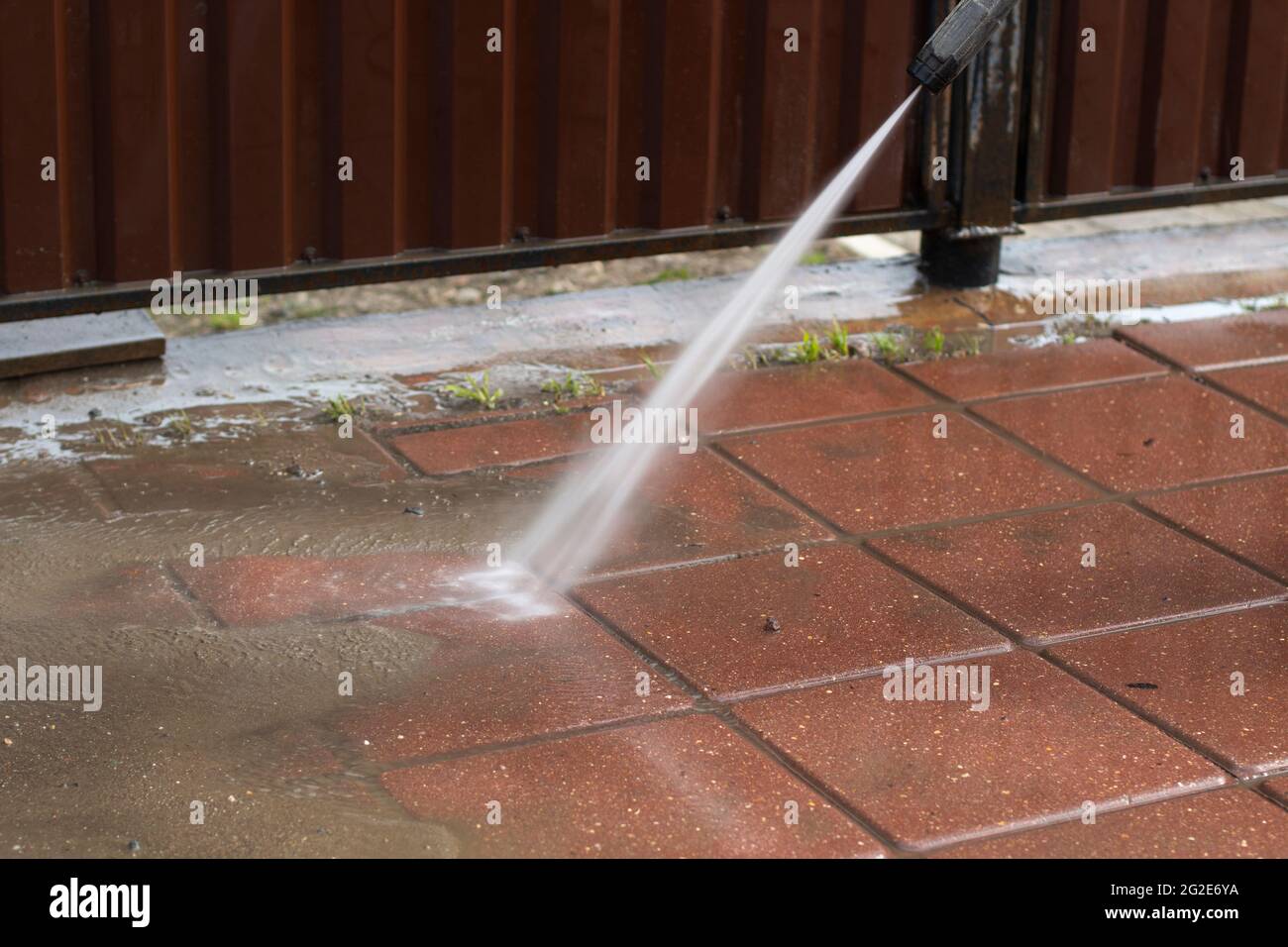 Lave le tapis roulant avec un jet d'eau. L'homme enlève la saleté du  chemin. Nettoyer la clôture et le trottoir de la poussière Photo Stock -  Alamy