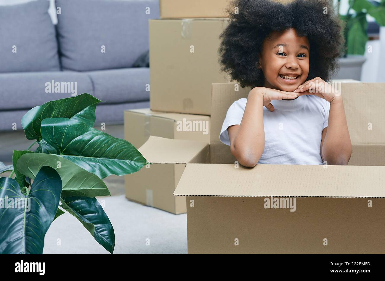 Bonne petite fille africaine américaine jouant avec des boîtes en carton, s'amusant tout en se déplaçant à la maison Banque D'Images