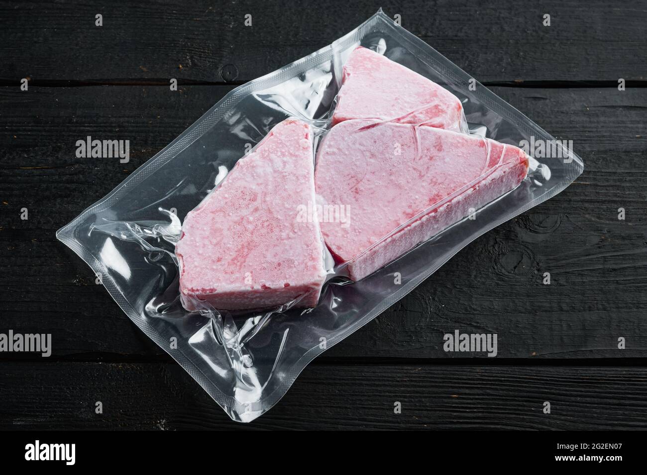 Steak de thon congelé dans un emballage en plastique sous vide, sur fond en  bois noir Photo Stock - Alamy
