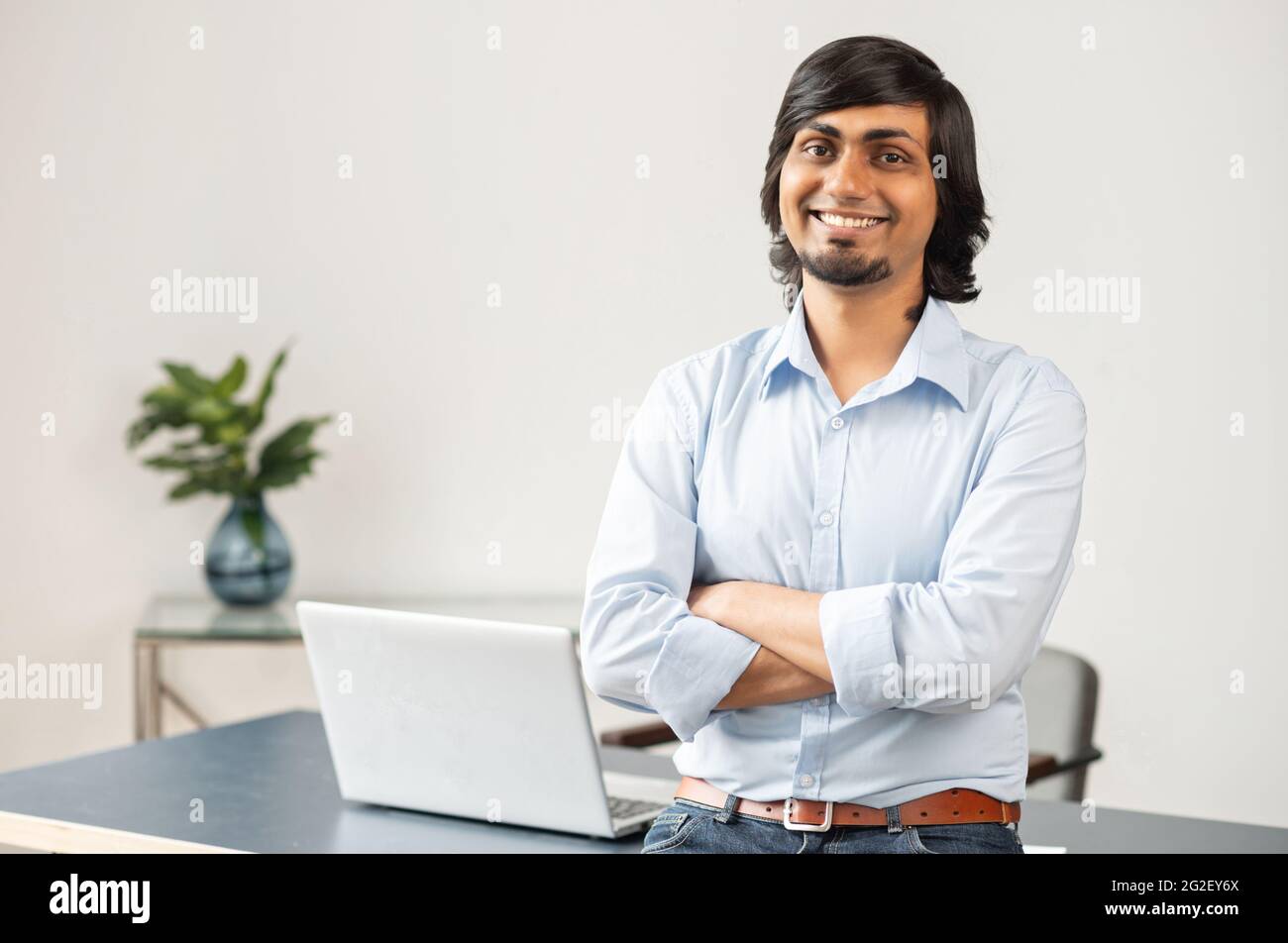 Un homme d'affaires indien ambitieux et hautement qualifié se pose en toute confiance dans un bureau moderne, un homme d'affaires de l'est souriant en tenue décontractée regarde la caméra avec les bras croisés. Succès et réalisation Banque D'Images