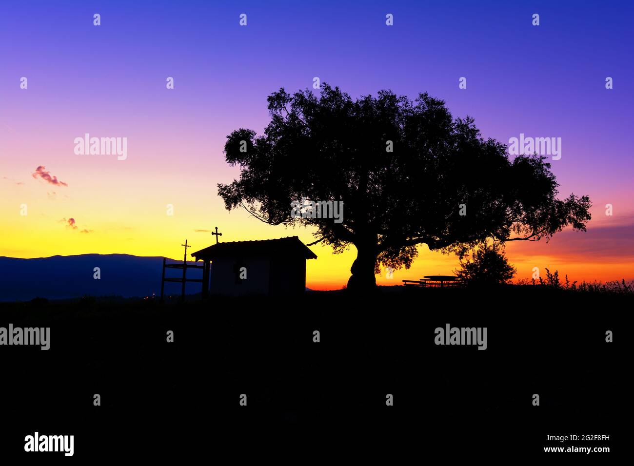 Silhouette de la chapelle chrétienne près du village de Plana, Bulgarie et un arbre avec une grande couronne à un coucher de soleil pittoresque. Banque D'Images