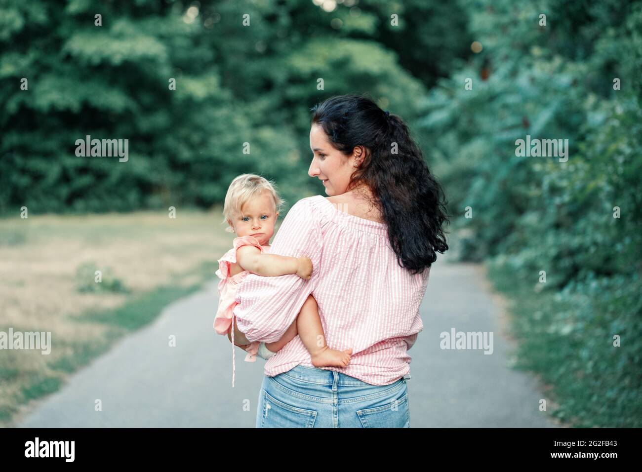 Fête des mères. Jeune mère caucasienne tenant porte fille petite fille fille sur son côté. Maman embrassant bébé enfant le jour d'été à l'extérieur. Heureux Banque D'Images
