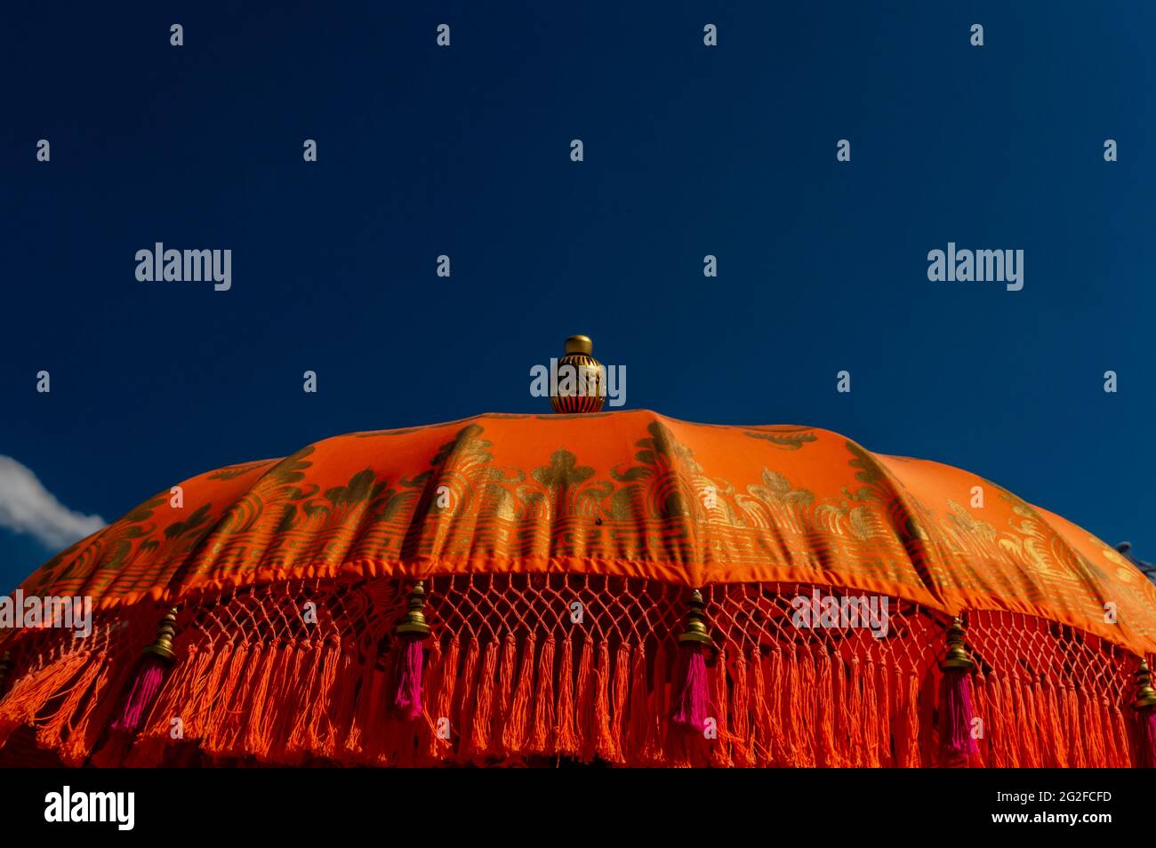 Un gros plan de parasol indien orange vif et or avec des glands roses contre un ciel bleu par une journée ensoleillée Banque D'Images